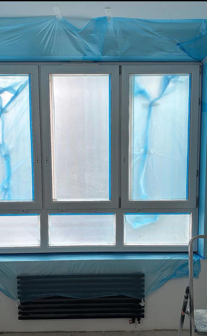 То же окно до работ: серый профиль, укрытый плёнкой и малярным скотчем